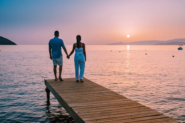 Kreta Grecja, młoda zakochana romantyczna para siedzi i przytula się na drewnianym molo na plaży o wschodzie słońca ze złotym niebem. Koncepcja wakacji i podróży. Romantyczna młoda para randkowa nad morzem — Zdjęcie stockowe