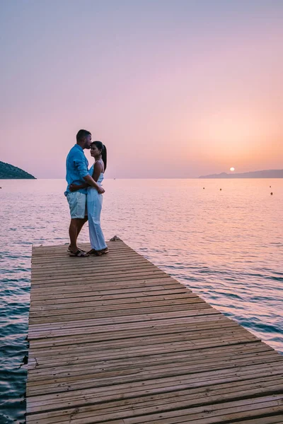 Girit Yunanistan 'da, birbirine aşık genç romantik çift gün doğumunda altın gökyüzü eşliğinde kumsaldaki ahşap iskelede oturup sarılıyor. Tatil ve seyahat konsepti. Deniz kenarında flört eden romantik genç çift — Stok fotoğraf