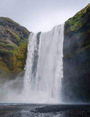 Skogafoss şelalesi, İzlanda 'nın yemyeşil yeşillikleriyle çevrili yüksek uçurumlardan gök gürültüsü gibi iniyor. Bu nefes kesici doğa harikası ziyaretçileri manzaralı yürüyüş yolları boyunca güzelliğini keşfetmeye davet ediyor..