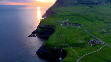 Mullafossur Şelalesi 'ni aydınlatan ve Gasadalur, Faroe Adaları' ndaki Atlantik Okyanusu 'na dökülen nefes kesici günbatımına tanık olun. Sakin manzarada yemyeşil ve engebeli uçurumlar var..