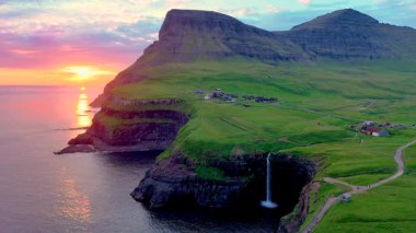 Mullafossur Şelalesi 'nin nefes kesici güzelliğine tanık olun. Bereketli yeşil uçurumlardan aşağı dökülüyor. Güneşin doğuşuyla Faroe Adaları' nın sakin suları üzerinde gökyüzünü aydınlatıyor..