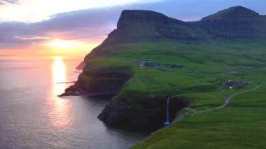 Güneş görkemli uçurumların ardında batarken Faroe Adaları 'ndaki Gasadalur' un çarpıcı manzarasını deneyimleyin. Huzurlu Mullafossur şelalesi okyanusa dökülür ve sakin bir atmosfer yaratır..