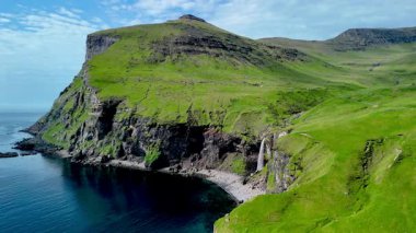 Faroe Adaları 'ndaki berrak sularda çarpıcı uçurumlar dramatik bir şekilde yükselir. Bereketli yeşillik manzarayı örtüyor. Bölgelerin bozulmamış cazibesini ve sakin atmosferini gösteriyor..