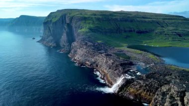 Sakin suların üzerinde yükselen dramatik uçurumlarla Faroe Adaları 'nın çarpıcı doğal güzelliğini keşfedin. Bu büyüleyici kıyı manzarası bu uzak yerin eşsiz jeolojisini gözler önüne seriyor..