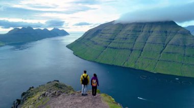 İki yürüyüşçü kayalık bir uçurumun kenarında durup Faroe Adaları 'nın nefes kesici manzarasına hayret ediyorlar. Bereketli yeşil dağlar, derin mavi Atlantik 'ten görkemli bir şekilde yükselirler ve sakin bir kaçış yaratırlar..