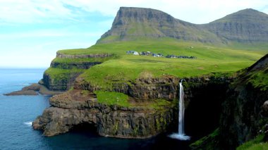 Büyüleyici Gasadalur Vadisi 'nde yuva yapmış Mullafossur Şelalesi, yemyeşil tepeler ve engebeli kayalıklarla çevrili olarak dramatik bir şekilde denize dökülüyor..