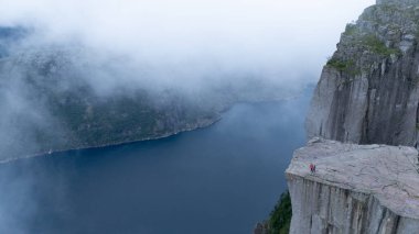 Preikestolen Cliff 'ten nefes kesici manzarayı keşfedin, Lysefjord' un aşağıdaki dramatik manzarasını ortaya çıkarın. Yalnız bir yürüyüşçü, gizemli sis ve dingin suların ortasında doğayı kucaklıyor..