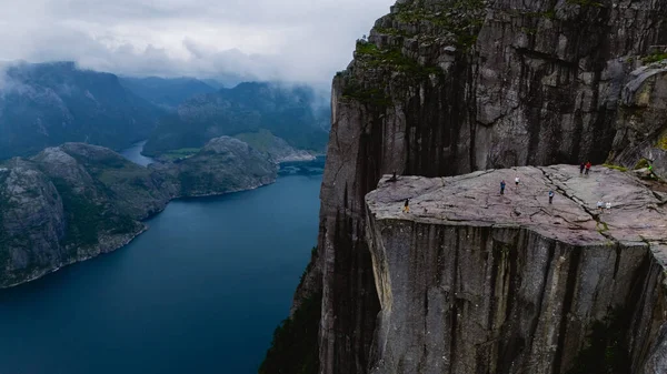 Preikestolen Cliff 'in geniş görüşleri Lysefjord' a dramatik bir bakış açısı sunuyor. Maceraperest yürüyüşçüler kasvetli bir gökyüzü altında büyüleyici doğal manzarayı keşfediyorlar..