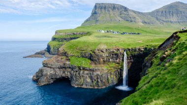 Su çarpıcı Mulafossur şelalesinden aşağı yuvarlanıyor, yemyeşil uçurumlarla çevrili, derin mavi Atlantik Okyanusuna dökülüyor..