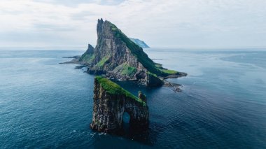 Towering Drangarnir uçurumları verimli yeşilliklerle çevrili. Faroe Adaları 'nın sakin, derin mavi okyanusunun üzerinde görkemli bir şekilde duruyorlar. Çarpıcı manzara bir sükunet ve macera hissi uyandırıyor..