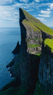 Görkemli uçurumlar Kuzey Atlantik Okyanusu 'nun üzerinde uçarak büyüleyici Faroe Adaları' nda doğal güzelliklerini sergilerler. Bereketli yeşil manzaralar, parlak bir gökyüzüne karşı engebeli kaya oluşumlarıyla tezat oluşturuyor..