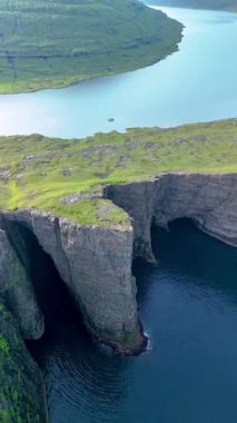 Faroe Adaları 'ndaki sakin sulara bakan yüksek uçurumların bulunduğu sakin bir manzara. Yeşil yamaçlar engebeli kıyı şeridiyle harmanlanarak Sorvagsvatn Gölü ve Vagar 'ın pitoresk manzarasını oluşturuyor.