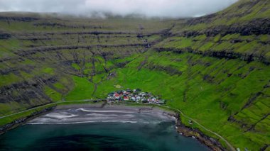 Yükselen kayalıkların arasına yerleşen Tjornuvik, büyüleyici köyünü ve Faroe Adaları 'nın kara kumsalını sergiliyor.