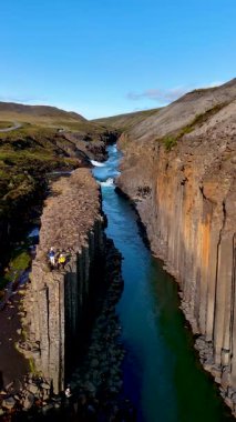 Studlagil Kanyonu 'nun çarpıcı jeolojik oluşumlarına tanık olun. Bazalt sütunları turkuaz suların yanında görkemli bir şekilde yükseliyor. İzlanda 'da tatilde olan birkaç erkek ve kadın.