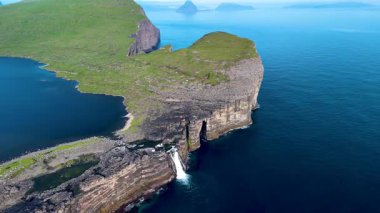 Faroe Adaları 'ndaki mavi sulardan yükselen görkemli uçurumlar büyüleyici doğal güzellikler sergiliyor. Bir şelale kayalık oluşumlardan aşağı yuvarlanır, sakin manzarayı somutlaştırır, Sorvagsvatn Gölü, Vagar