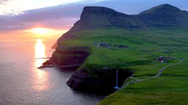 Şelalenin dramatik bir günbatımı altında denize döküldüğü Gasadalur 'daki Mullafossur manzarasını keşfedin. Faroe Adaları 'nın cazibesini tecrübe et..