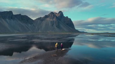 Kaşifler, Vestrahorn 'un eşsiz kara kumlu sahilinde dikilip alacakaranlıkta canlı bir gökyüzünün altındaki sakin sulara yansıyan görkemli dağa bakarak İzlanda doğasının güzelliğini yakalıyorlar..