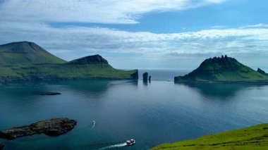 Sakin suların üzerinde dramatik uçurumların yükseldiği Faroe Adaları 'nın çarpıcı güzelliğini keşfedin. Bir tekne, yemyeşil dağlar ve el değmemiş bir okyanusla çevrili sakin bir arazide gezinir..