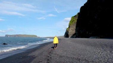 Reynisfjara Sahili 'nin eşsiz siyah kumlarında dramatik uçurumlar ve canlı mavi okyanuslarla çevrili bir kadın geziniyor. İzlanda 'daki bu pitoresk konum İzlanda' nın nefes kesici manzarasını sunuyor