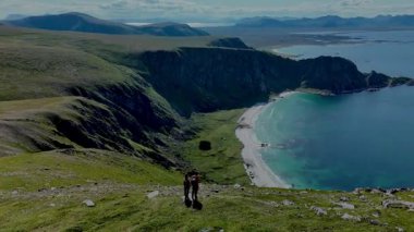 Kaşifler yemyeşil bir yamaçtan Norveç kıyısındaki sakin bir plaja doğru ilerliyorlar. Manzara heybetli uçurumları, berrak suları ve dalgalı bir gökyüzünün altında yuvarlanan tepeleri sergiliyor..