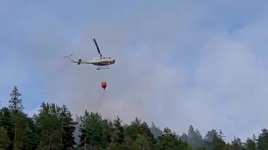Norveç 'teki bir orman yangınını söndürmek için yorulmadan çalışan su damlası sistemli bir helikopter görülüyor..