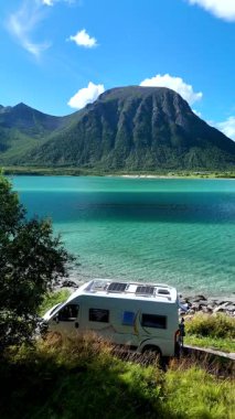 Lofoten Norveç 'in sakin turkuaz suları boyunca park etmiş, görkemli dağlar ve yemyeşil alanlar tarafından çerçevelenmiş bir karavan. Macera arayanlar ve doğa severler için mükemmel..