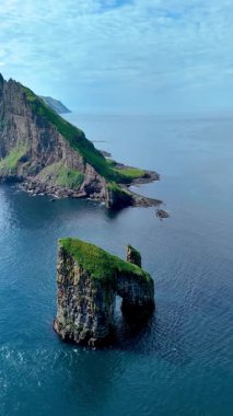Faroe Adaları 'nın sakin sularından çıkan Drangarnir kaya oluşumunun nefes kesici görüntüsü. yemyeşil manzaralar görkemli bir şekilde yükselir okyanusun dingin arkaplanına karşı.