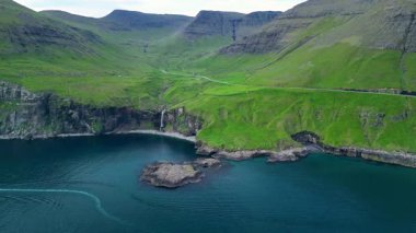 Faroe Adaları 'nın göz kamaştırıcı güzelliğini, yemyeşil tepeler ve görkemli uçurumlar boyunca tecrübe edin. Sakin bir şelale dingin mavi sulara dökülür ve güzel bir manzara yaratır..