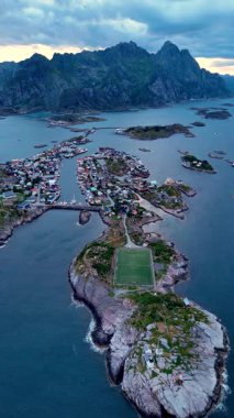 Norveç 'in Lofoten kentindeki muhteşem Henningsvaer köyünü kaplayan güzel bir hava manzarası kayalık manzaralar, sakin sular ve alacakaranlıktaki görkemli dağların altında yuva yapmış rahat evler sergiliyor..