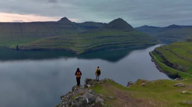 İki yürüyüşçü bir uçurumun kenarında durup fiyortun sakin sularına bakıyorlar. Gonguturur Hvithamar Faroe Adası