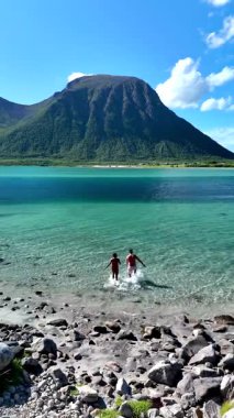 İki arkadaş Norveç 'in berrak, turkuaz sularında sersemletici kıyı şeridine sıçrarken yazın verdiği hazzı hissedin. Güneşli bir günde arka planda nefes kesici dağlar görkemli bir şekilde yükselir..