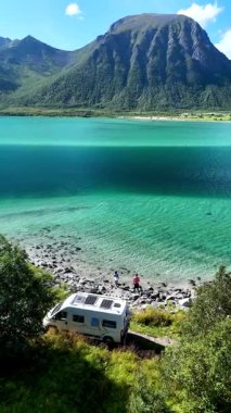 Lofoten Norveç 'teki kristal berrak turkuaz sularda park etmiş bir karavanın sakin manzarası doğal manzarayı sersemletiyor. Görkemli dağlar ve bereketli yeşillik huzurlu manzaranın etrafını sarar.