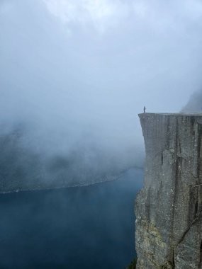 Yalnız bir figür sis ve sis perdesine karşı durduğu için, Preikestolen Cliff 'in dramatik güzelliğini deneyimleyin. Aşağıdaki görkemli Lysefjord büyüleyici atmosfere katkı yapıyor..