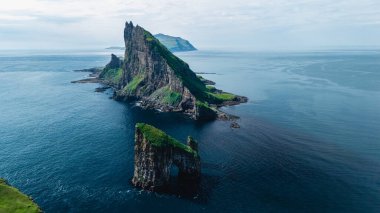 Faroe Adaları 'ndaki Drangarnir kaya oluşumları sakin Atlantik sularından sarsılıyor. Bereketli yeşillik, gün ortasında nefes kesici bir kıyı manzarası yaratan engebeli kayalıklarla çelişiyor..