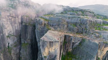 Preikestolen Cliff 'te, maceracılar aşağıdaki Lysefjord' un nefes kesici manzarasına hayranlıkla bakıyorlar. Bu ikonik doğa simgesi dramatik uçurumlar ve yemyeşil alanlar gösteriyor..