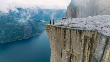 Norveç 'teki muhteşem Lysefjorden fiyorduna bakan ikonik Preikestolen uçurumunun üzerinde iki yürüyüşçü duruyor..