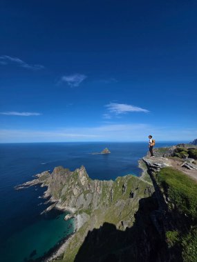 Bir yürüyüşçü, Andoya Adası 'ndaki Bleik yakınlarındaki Norveç Denizi' nin masmavi suları ve dramatik uçurumlarla çevrili Matind Dağı 'ndan çarpıcı panoramik manzaranın keyfini çıkarıyor..