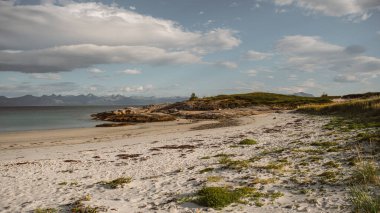 Norveç 'in Lofoten kentindeki Bognes' in sakin sahil şeridini keşfedin. Yumuşak kumlu plajlar yemyeşil manzaralarla buluşur. Dramatik bir gökyüzünün altında görkemli dağlar yükseliyor..