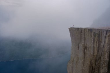 Preikestolen Uçurumunun kenarında duran yalnız bir figür dramatik sis ve sarp kayalıklarla çevrili. Aşağıdaki çarpıcı fiyort Norveç 'in bu ikonik manzarasına bir macera hissi katıyor..