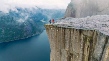 Preikestolen Uçurumunun kenarında duran iki yürüyüşçü Norveç 'te muhteşem bir fiyorda bakıyorlar. Sabah sisi peyzajı yumuşatarak sakin ve görkemli bir atmosfer yaratıyor..
