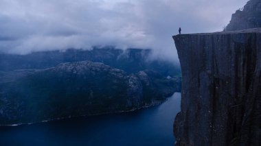 Preikestolen Cliff 'ten büyüleyici bir alacakaranlık görüntüsü, Norveç fiyortlarına ve yüksek manzaralara dramatik bir perspektif sunuyor. Uçurumun kenarında duran yalnız bir yürüyüşçü, ihtişamı kucaklıyor..