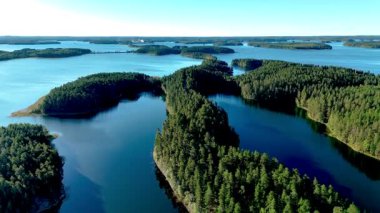 Finlandiya, Punkaharju 'da yemyeşil ormanların kristal berrak göllerle buluştuğu büyüleyici güzelliği keşfedin. Punkaharju Doğa Koruma Alanı 'ndaki bir göl ve yeşil orman arasındaki doğal bir yolda insansız hava aracı görüntüsü 