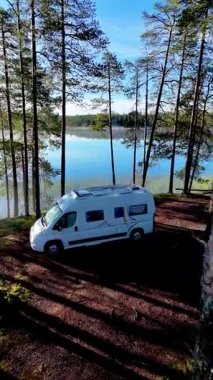 Finlandiya ormanlarındaki gölün kıyısında, Hossa Ulusal Parkı 'nda yüksek ağaçlar ve sakin sularla çevrili bir karavan. Finlandiya 'da kamp ve açık hava maceraları için ideal bir yer..