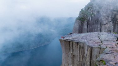 Maceracılar muhteşem Lysefjorden 'a tepeden bakan Preikestolen Cliff' in kenarında dururlar. Sis zerreleri, Norveç 'in görkemli güzelliğini artıran ruhani bir atmosfer yaratıyor..