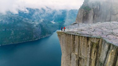 İki maceracı Preikestolen Cliff 'in kıyısında dururken Lysefjord' un sakin sularından heybetli uçurumlar keskin bir şekilde yükselir..