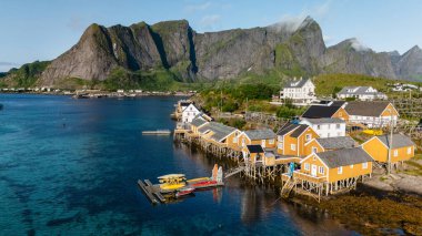 Sakrisoy, Lofoten, Norveç 'te açık mavi bir gökyüzünün altında dramatik tepelere vuran renkli rorbu kulübeleri. Bu pitoresk köy İskandinav güzelliğinin özünü yansıtıyor..