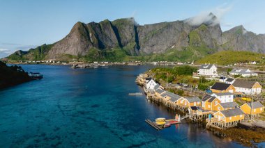 Norveç 'in Lofoten kentindeki Sakrisoy köyünün göz kamaştırıcı güzelliğini görün. Renkli kulübelerin dingin suları berrak bir gökyüzünün altındaki görkemli dağların zeminine çizdiği yer..