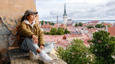 Asyalı kadın Estonya 'nın Tallinn şehrinde huzurlu bir manzaranın tadını çıkarıyor. Tarihi mimari ve bereketli yeşillik Baltık Denizi 'ne karşı büyüleyici bir zemin hazırladı..
