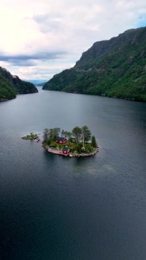 Lovrafjorden Norveç 'teki uzak bir adanın göz kamaştırıcı manzarası. Yeşillikler arasında canlı kırmızı kulübeler var. Sakin sular etkileyici dağ manzarasını yansıtıyor.