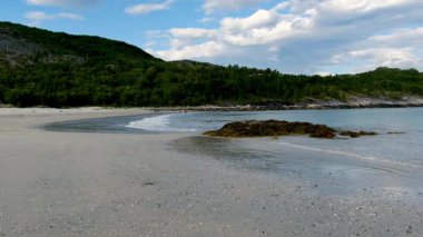Lofoten, Norveç 'teki Mannen Haukland' ın sakin kıyılarını deneyin. Yumuşak dalgalar arka planda yemyeşil tepeler yükselirken kumlu kumsalda nazikçe tur atar ve barışçıl bir atmosfer yaratır..